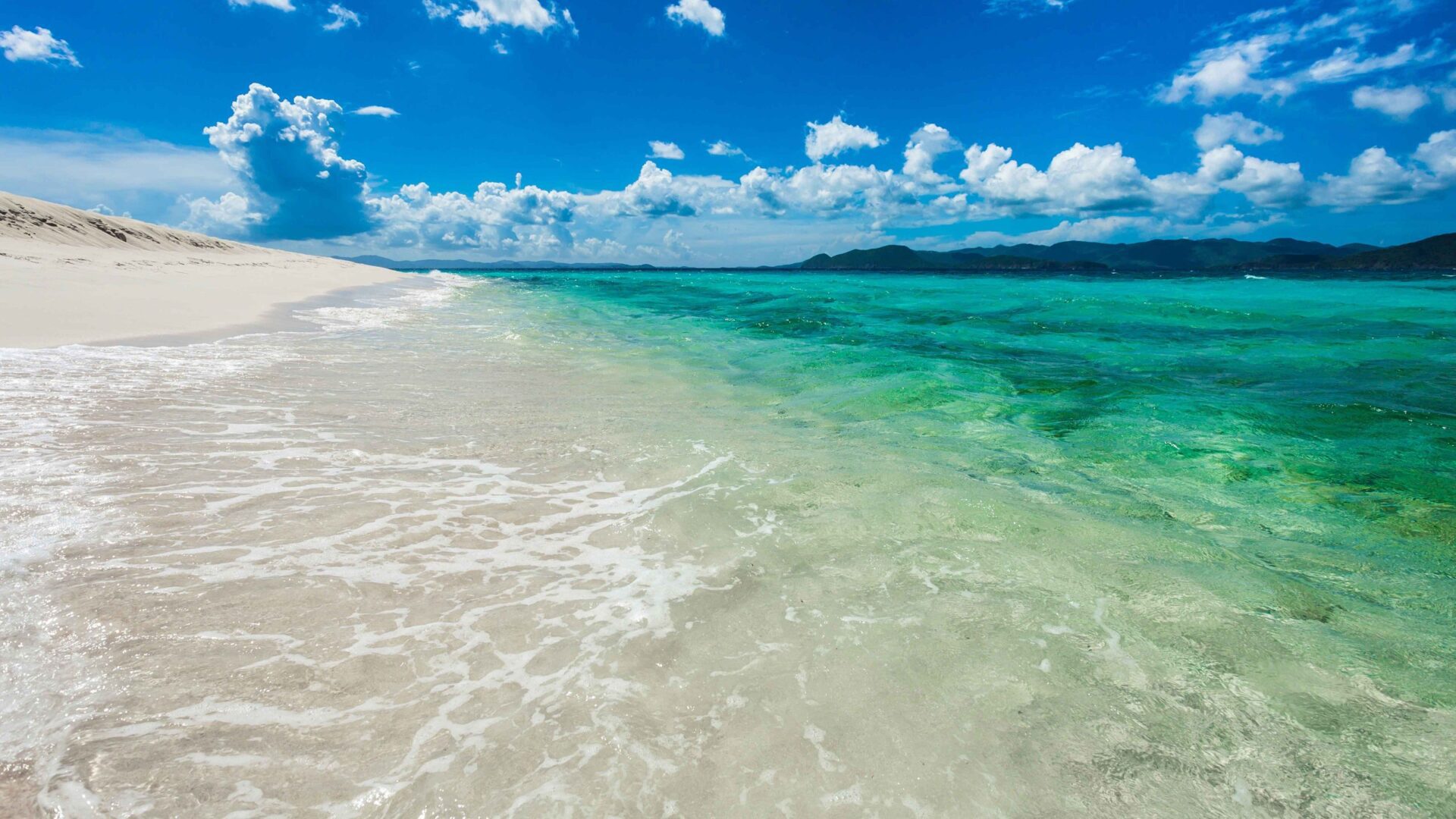 A beach with white sand and green water.