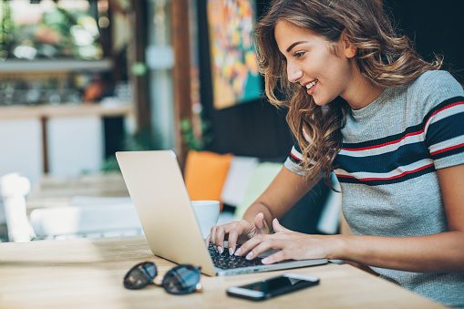 A woman is smiling while using her laptop.