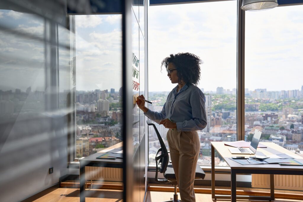 Woman standing near office window, looking outside thoughtfully.