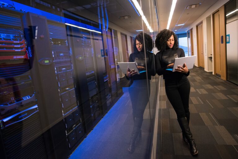 Woman working on laptop in a modern server room with glass walls.