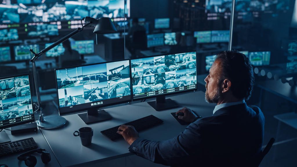 Man monitoring multiple surveillance screens in a control room.